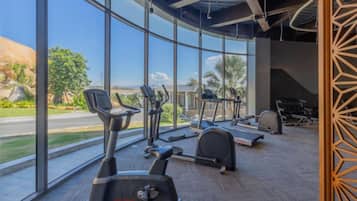 A gym with cardio equipment and large windows offering a view of the outdoors.