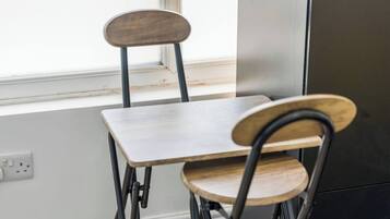 Een eethoek met een tafel en twee stoelen, een raam en een wandcontactdoos.