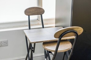 A dining area with a table and two chairs, a window, and a wall-mounted electrical outlet. - Modern Studio Apartment A with Self Check-In & Fast WiFi in Ilkeston (Derbyshire)