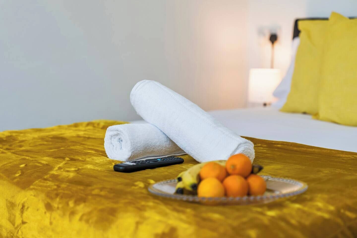 Un lit avec une couverture jaune, une télécommande et un bol de fruits.