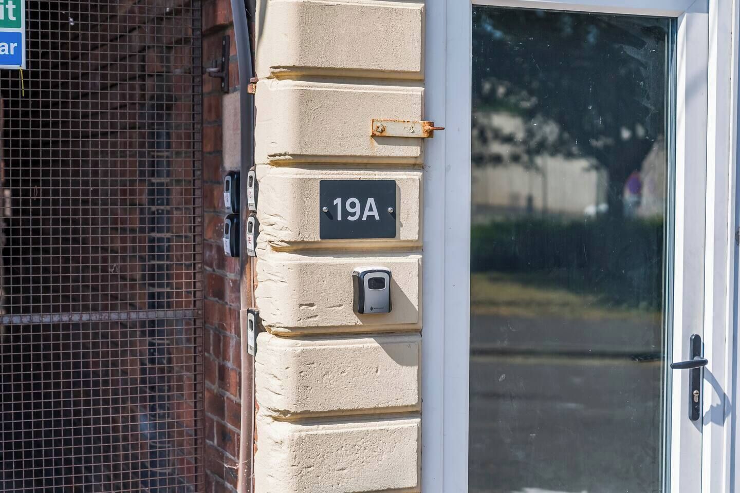 Entrada de un edificio con puerta, buzón y placa con el número de la casa.