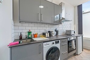 A compact kitchen with grey cabinets, a washing machine, a microwave, and a toaster. - Modern Studio Apartment A with Self Check-In & Fast WiFi in Ilkeston (Derbyshire)