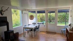 Una habitación con piso de madera, una mesa con sillas, una chimenea y ventanas amplias.