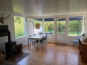 Ein Zimmer mit Holzboden, einem Tisch mit Stühlen, einem Kamin und großen Fenstern.