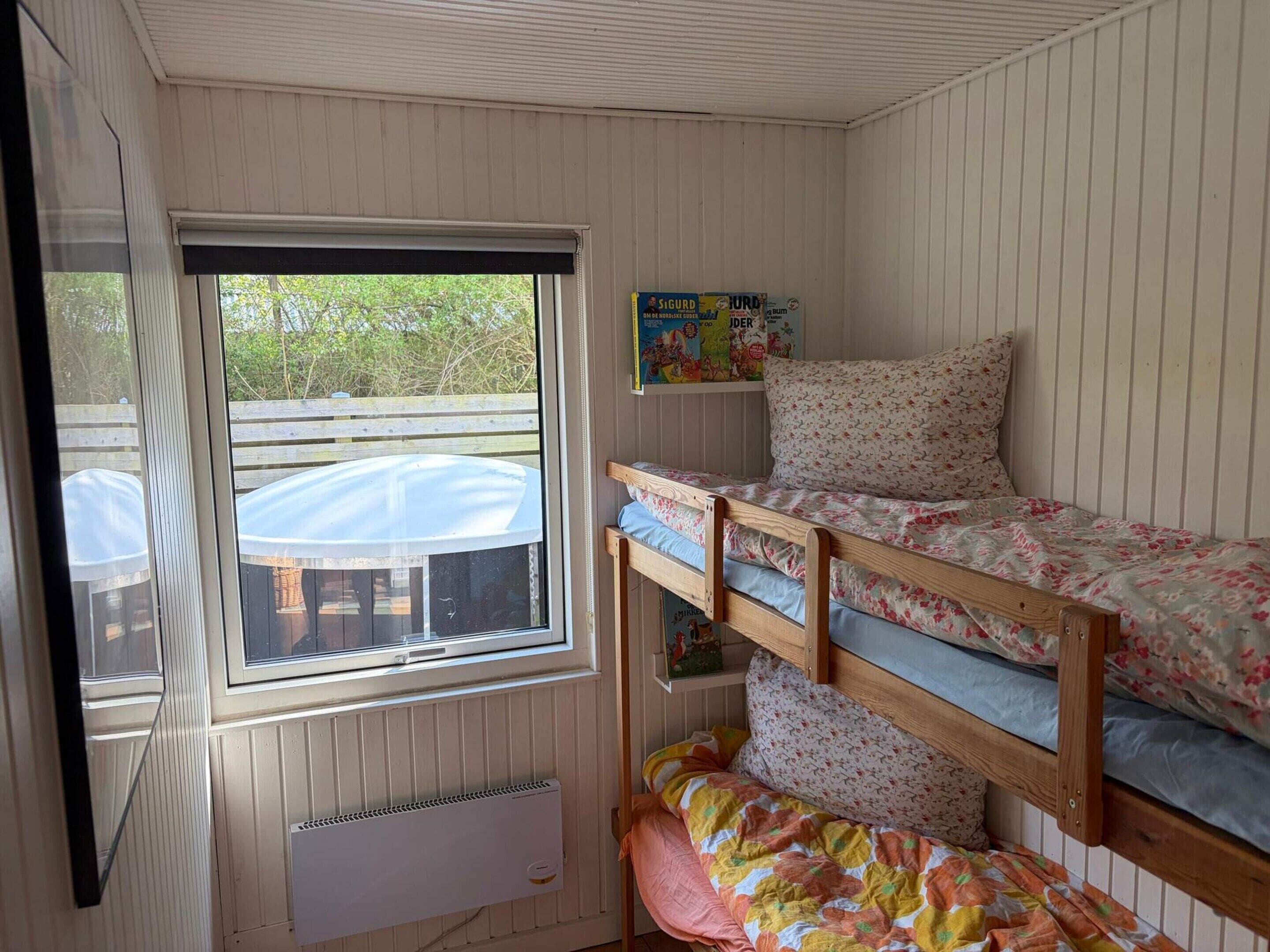 A bunk bed room with a window, a radiator, and a shelf with children's books.