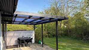 Un patio techado con una parrilla, asientos exteriores y vista a un jardín trasero.