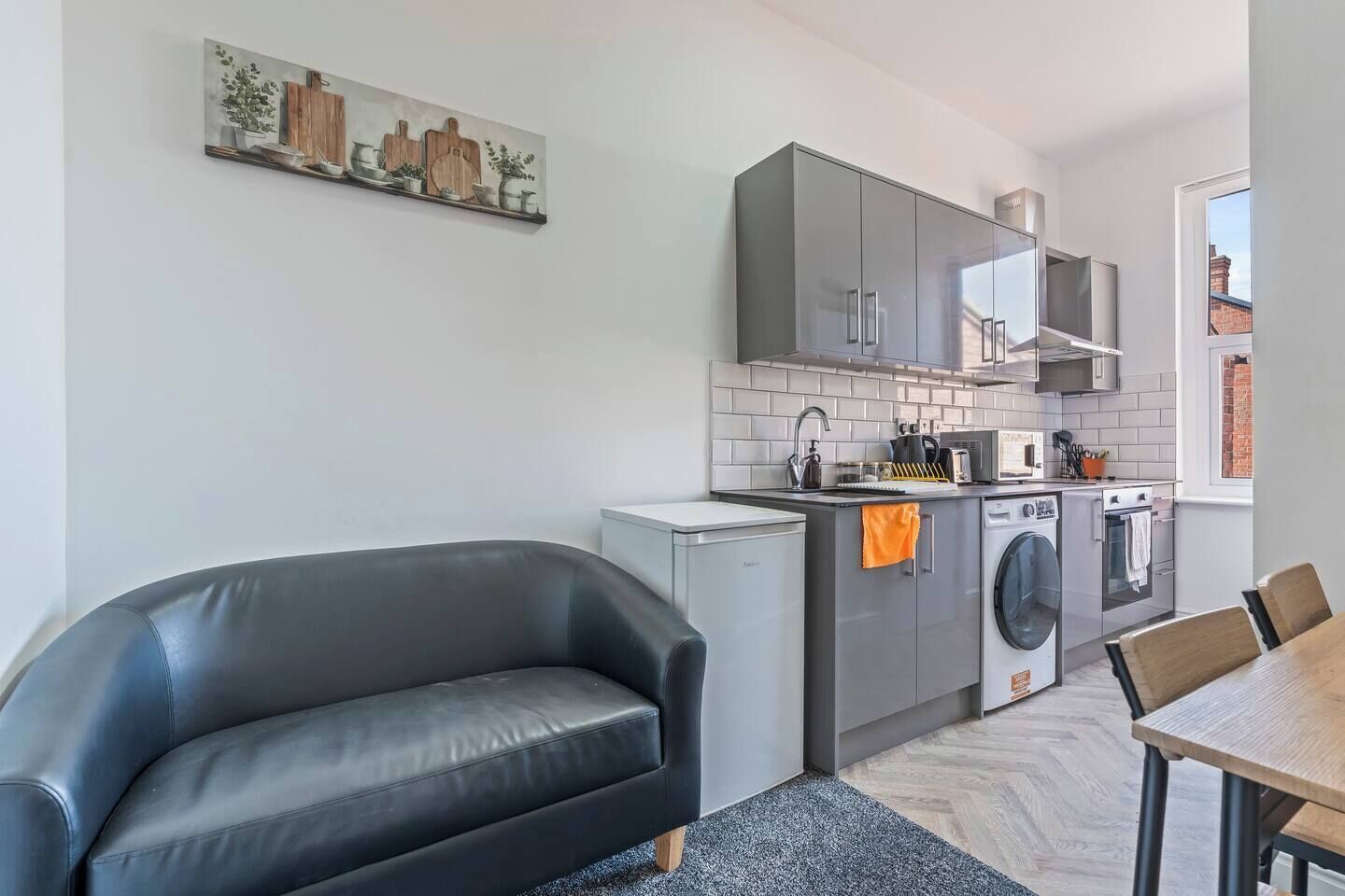 Een moderne keuken met grijze kastjes, een wasmachine en een eethoek met een tafel en stoelen.