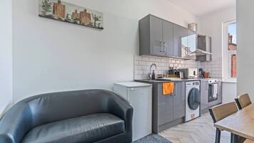 Een moderne keuken met grijze kastjes, een wasmachine en een eethoek met een tafel en stoelen.
