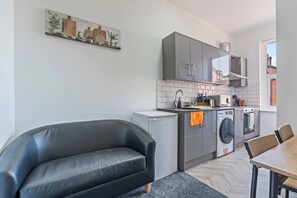 Eine moderne Küche mit grauen Schränken, einer Waschmaschine und einem Essbereich mit Tisch und Stühlen.