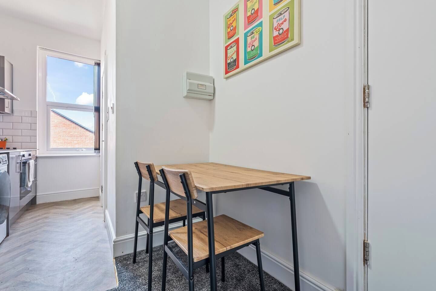 Et lille køkken med spisebord og stole, et vindue samt en vægmonteret stikkontakt.
