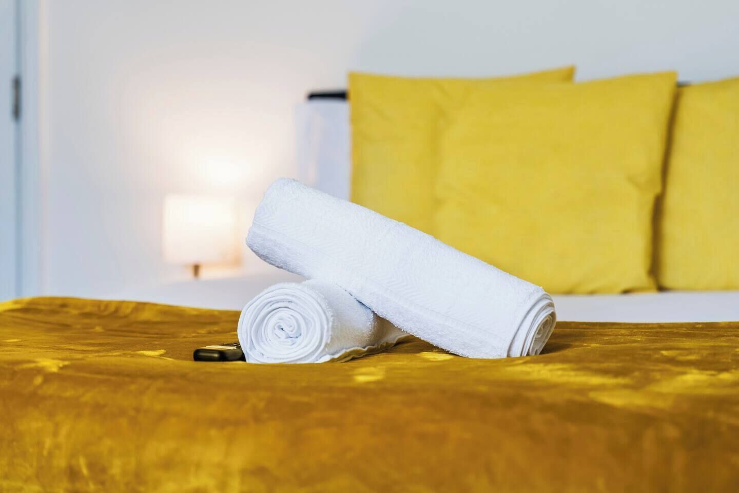 Ein Bett mit gelber Kopfteil, einem weißen Handtuch und einer Fernbedienung auf einer Holzoberfläche.