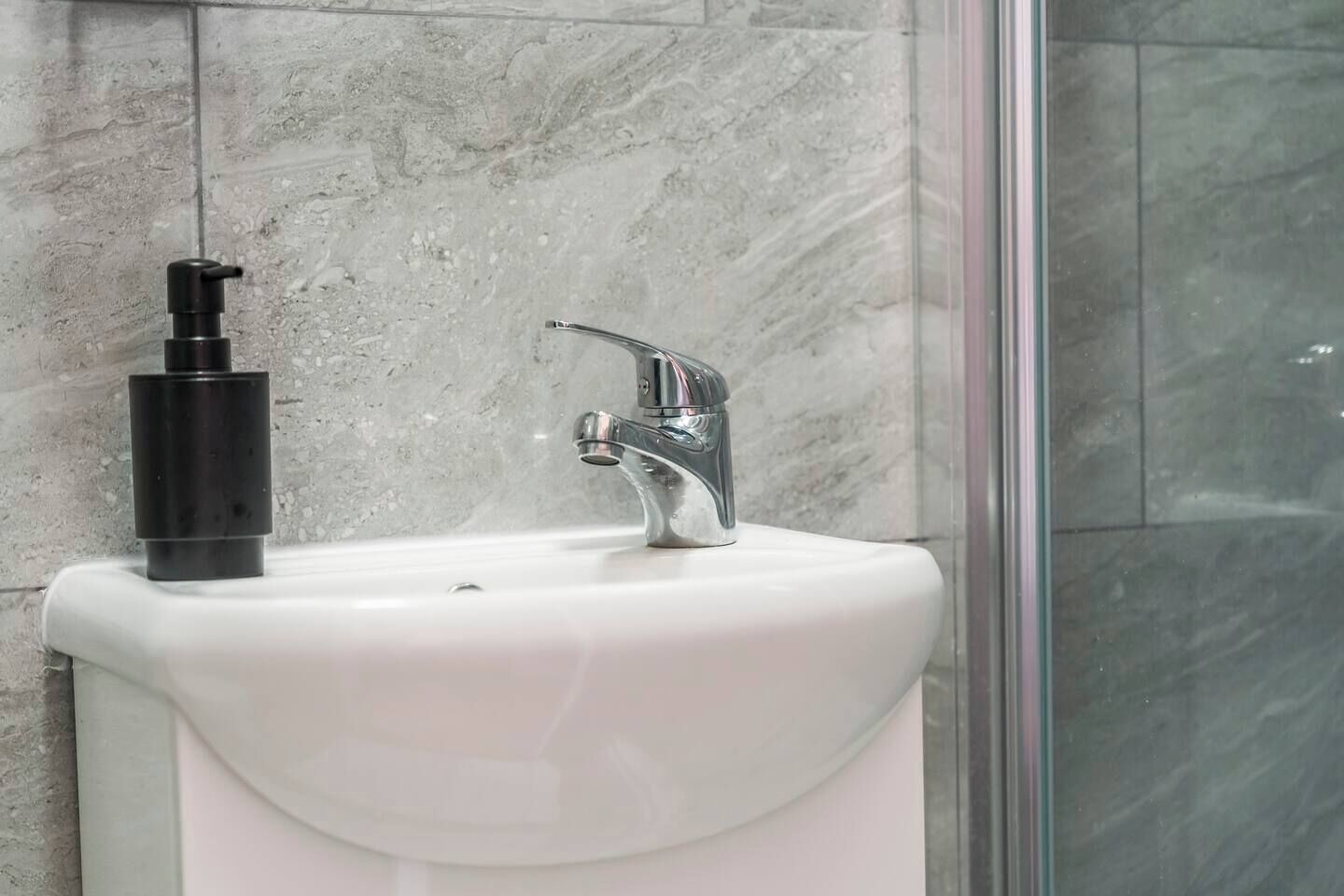 Un bagno con un lavandino bianco, un erogatore di sapone nero e un rubinetto cromato.
