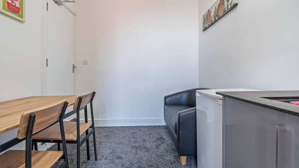 Et kompakt tekøkken med køleskab, vask og spiseplads med bord og stole.