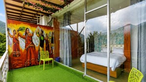 A room with a bed, a green artificial grass floor, a glass wall, and a mural on the wall.