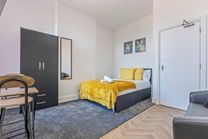 Un dormitorio con cama, escritorio, armario y puerta.