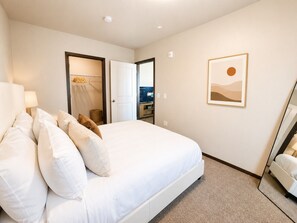 Ett hotellrum med en säng, ett sängbord, en lampa, en garderob och en inramad tavla på väggen.