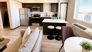A modern kitchen with a refrigerator, microwave, and stove, a dining area with a table and bar stools, and a living room with a sofa and a coffee table. - Stylish 2BR Tacoma Stay | Near Hospitals & Tacoma Dome (Tacoma)