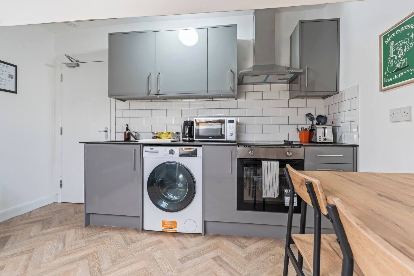 A compact kitchen with grey cabinets, a built-in washing machine, a microwave, and a toaster.