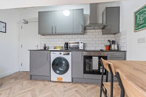Una cocina compacta con armarios grises, lavadora integrada, microondas y tostadora.