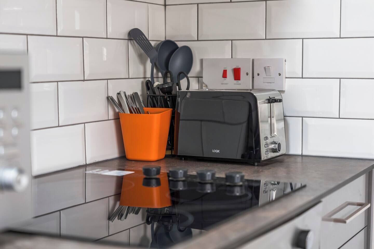 Et moderne køkken med en sort toaster, en samling knive i en orange holder og en komfur med kontrolknapper.