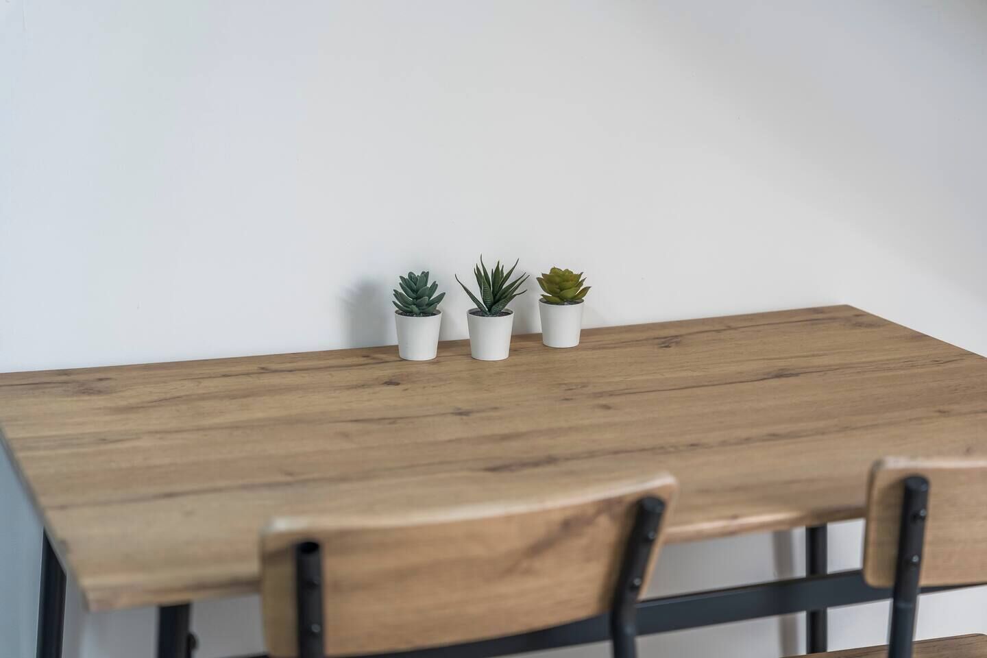 Una mesa de madera con tres plantas en macetas y dos sillas.