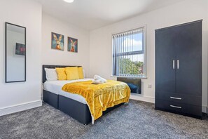 A bedroom with a bed, a wardrobe, a window with a view, and two paintings on the wall. - Top Floor Studio Apartment with Skylight & Fast WiFi in Ilkeston (Derbyshire)