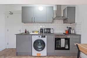 A compact kitchen with a washing machine, microwave, and a small oven. - Top Floor Studio Apartment with Skylight & Fast WiFi in Ilkeston (Derbyshire)