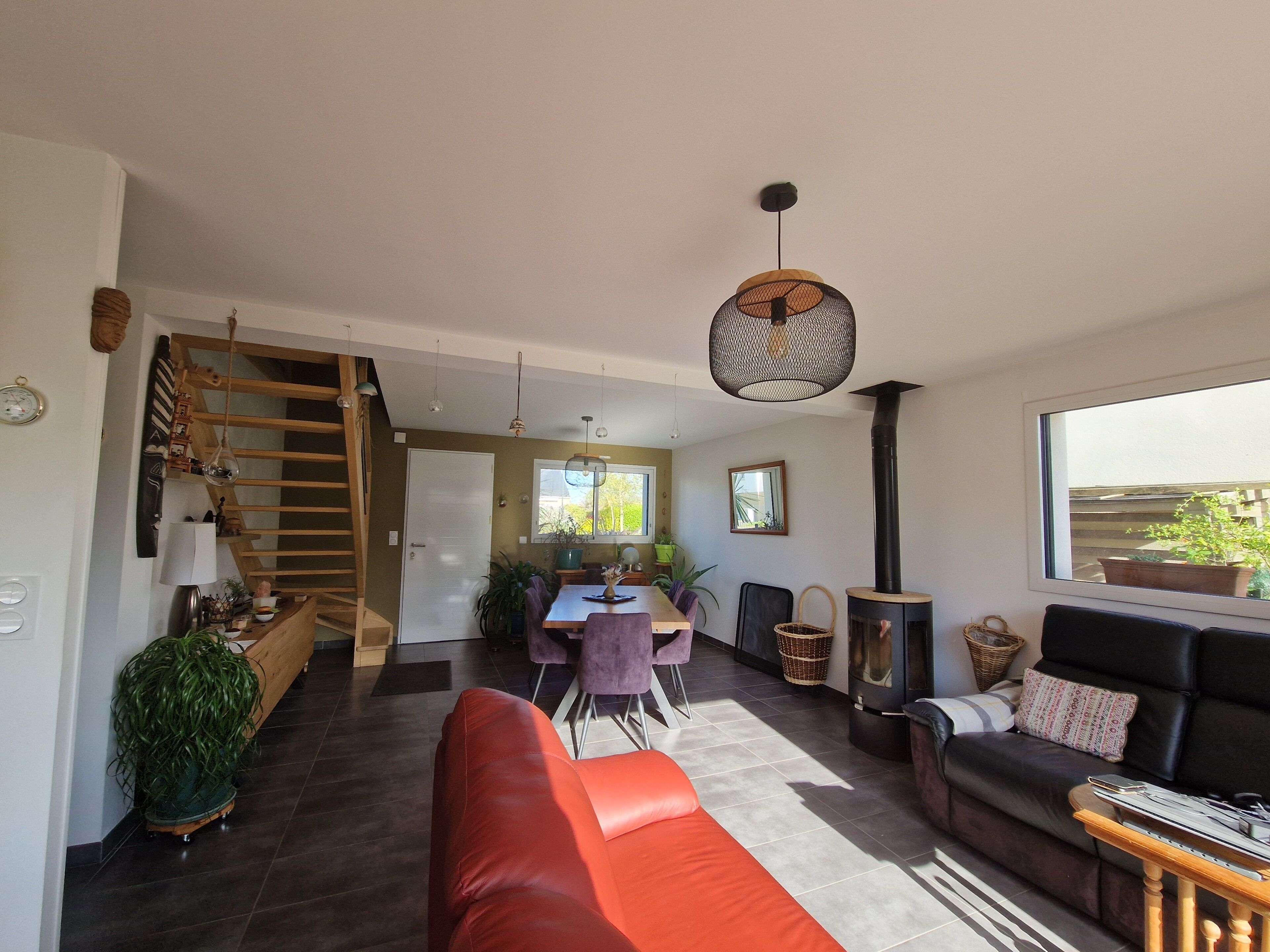 A modern living room with a sofa, dining area, staircase, and a large window.