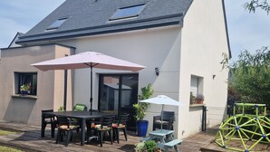 Ein modernes Haus mit Terrasse, einem Esstisch und Stühlen sowie einem großen Sonnenschirm.