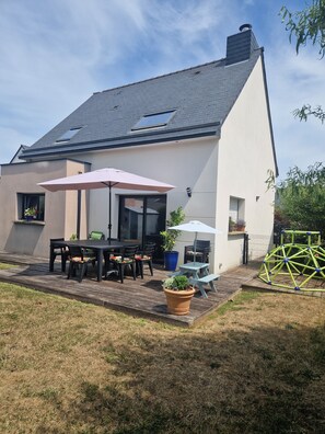 Ein modernes Haus mit Terrasse, einem Esstisch und Stühlen sowie einem großen Sonnenschirm.