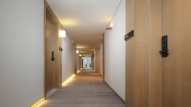 A hotel hallway with carpeted floors, wooden doors, and illuminated wall sconces.
