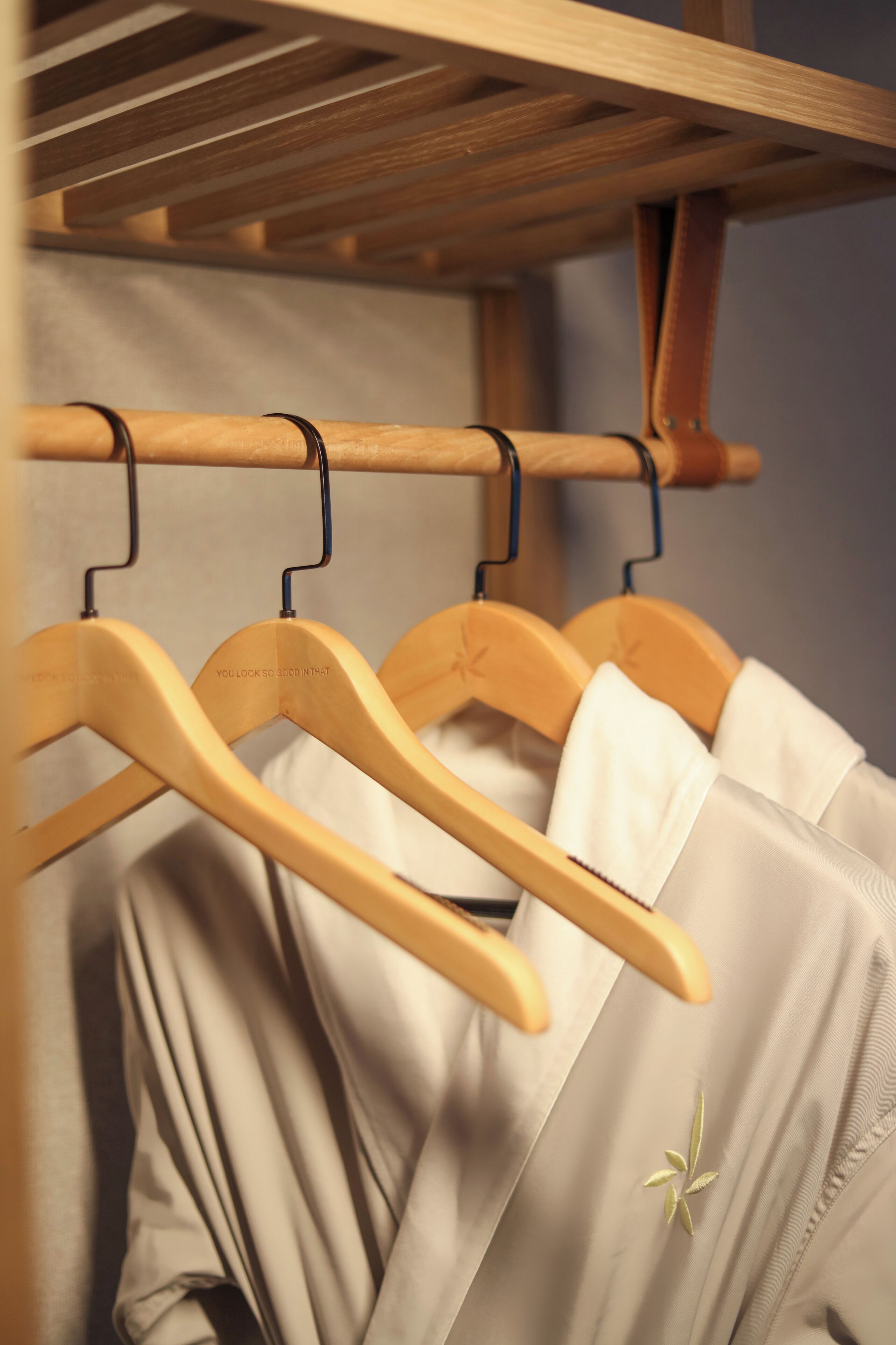 A wooden hanger rack with three hangers, each holding a white garment.