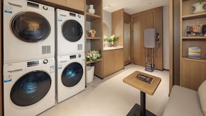 A hotel room with a built-in washer and dryer, a small table with a book, a mirror, and a shelf with decorative items.