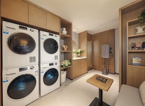 A hotel room with a built-in washer and dryer, a small table with a book, a mirror, and a shelf with decorative items.