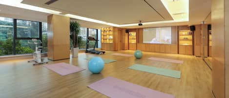 Un gimnasio moderno con equipo de ejercicio, colchonetas de yoga y un ventanal con vistas a la ciudad.