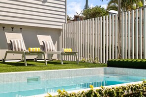 Ein Swimmingpool mit zwei Liegestühlen und einem weißen Zaun im Hintergrund.