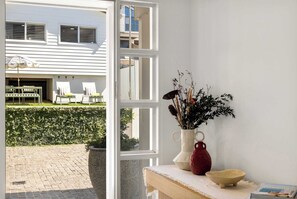 Ein Zimmer mit Blick auf ein weißes Gebäude, einer Topfpflanze und einer Vase mit Trockenblumen.