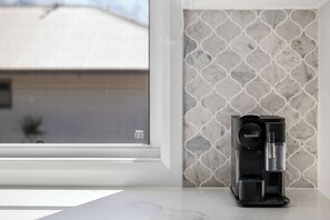 A Nespresso coffee machine on a countertop with a patterned backsplash and a window view. - Coolum Beach Coastal Retreat- Sleeps 10 (Coolum Beach)
