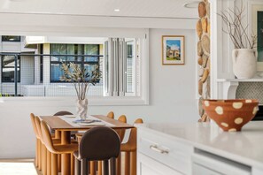 Eine moderne Küche mit weißen Schränken, einem Esstisch mit Stühlen, einer Vase mit Zweigen und einem gerahmten Bild an der Wand.