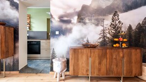 A kitchen with a wooden cabinet, a stove, and a dining area with a wooden table and a decorative fruit stand. - Grünstein Vacation Rental (Schönau am Königssee)