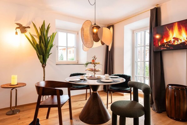 A dining area with a round table, chairs, a hanging light fixture, a plant, and a fireplace. - Grünstein Vacation Rental (Schönau am Königssee)