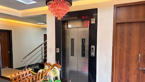 A lobby with a wooden bench, a chandelier, an elevator, and a door.
