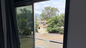 A view from a balcony with a glass door, overlooking a parking area and a building with a red roof.