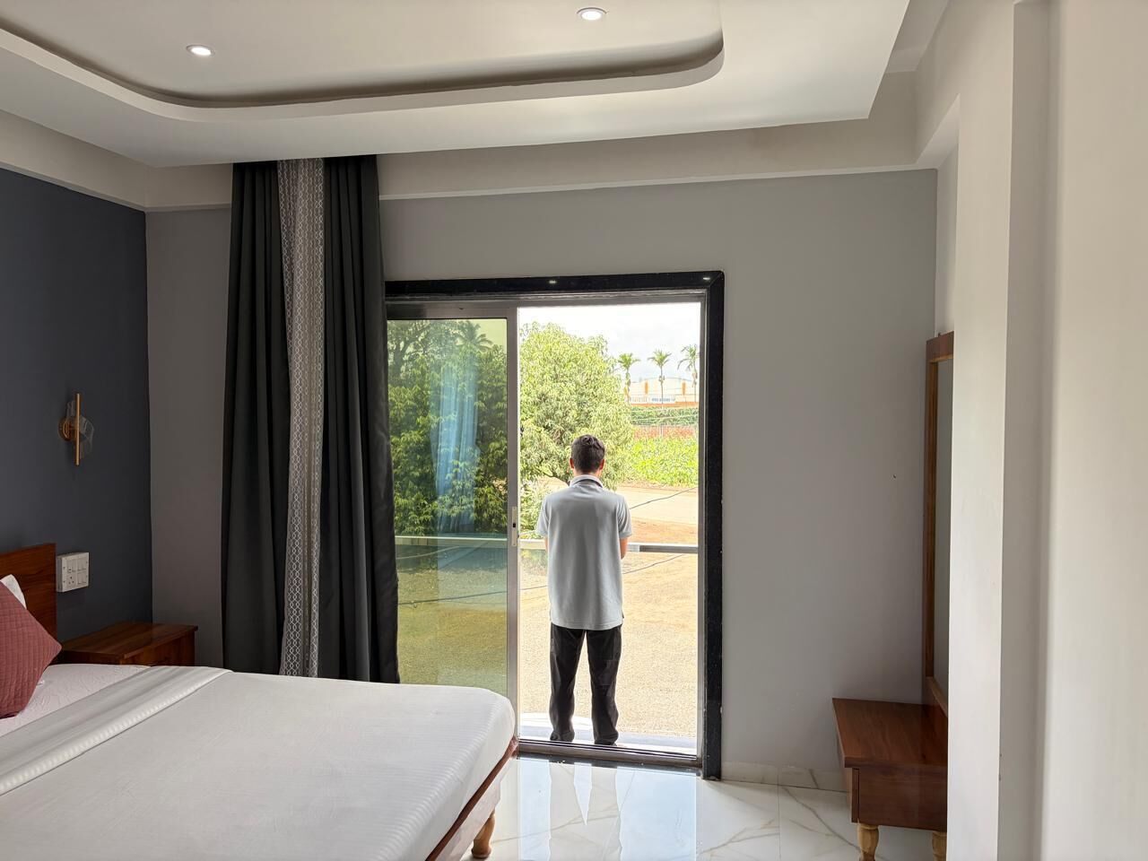 Un dormitorio con cama, mesita de noche, un ventanal con cortinas y vistas al exterior.
