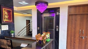 A hotel lobby with a reception desk, a staircase, a chandelier, and a wooden door.