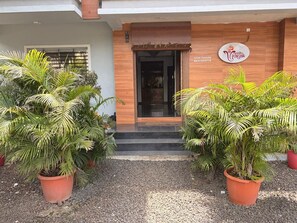 A building entrance with a wooden facade, a signboard, and potted plants.