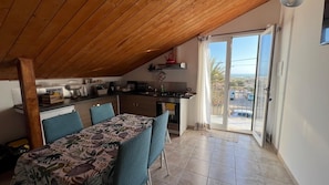 A dining area with a table and chairs, a kitchen in the background, and a sliding glass door leading to an outdoor area. - Casa Genisi - Vacations in Scicli (Genovese)