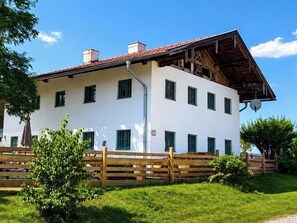 A white building with a sloped roof, multiple windows, and a wooden fence in front.