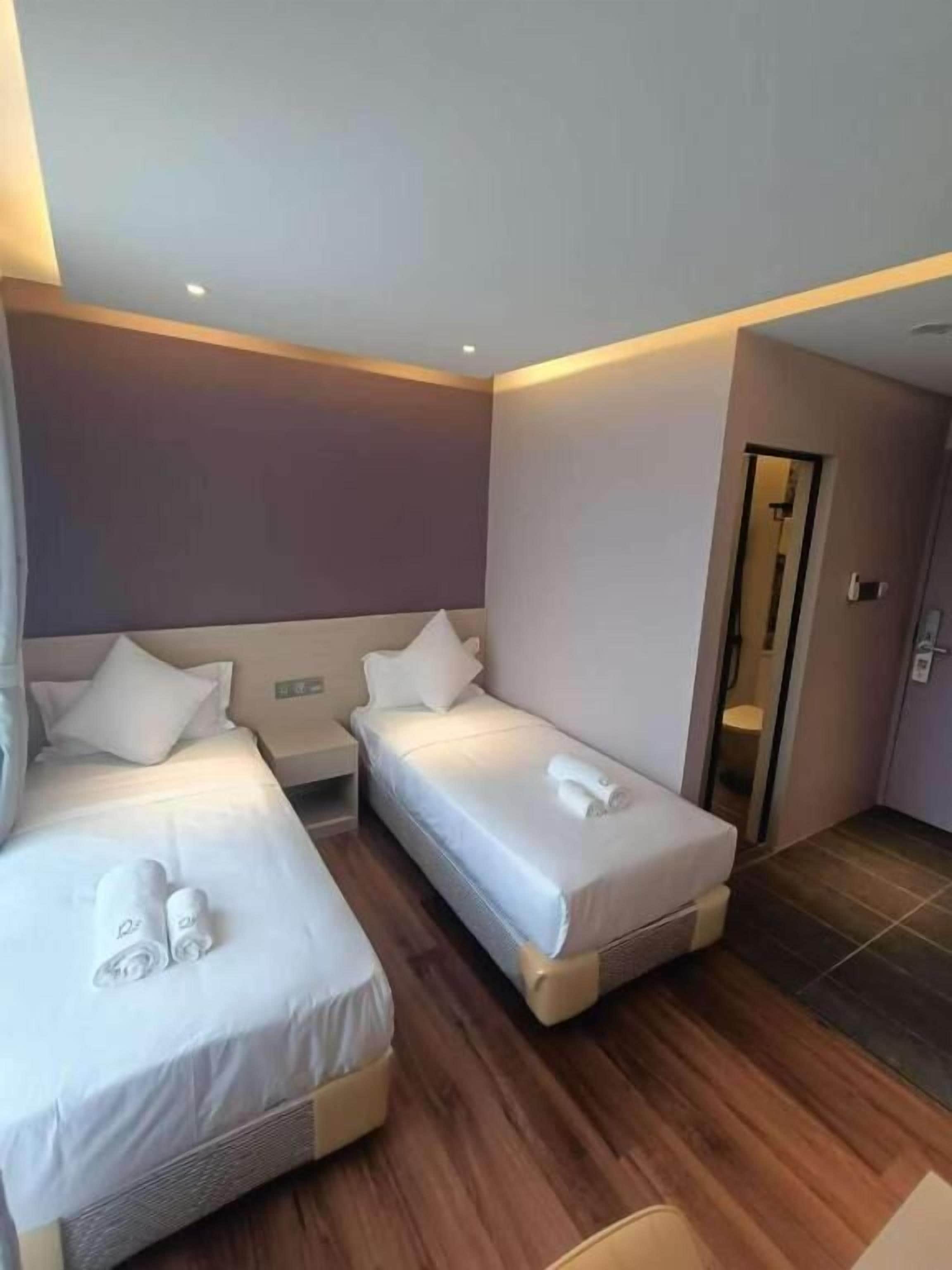 A hotel room with two single beds, a wooden floor, a small bedside table, and a door leading to a bathroom.