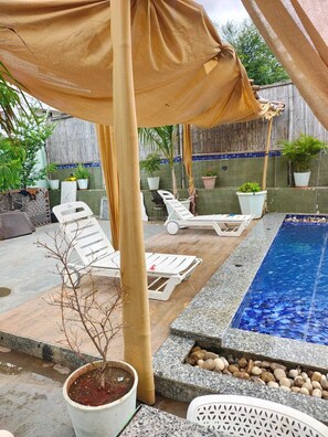 Ein Poolbereich mit Liegestühlen, einer Pergola und Topfpflanzen.